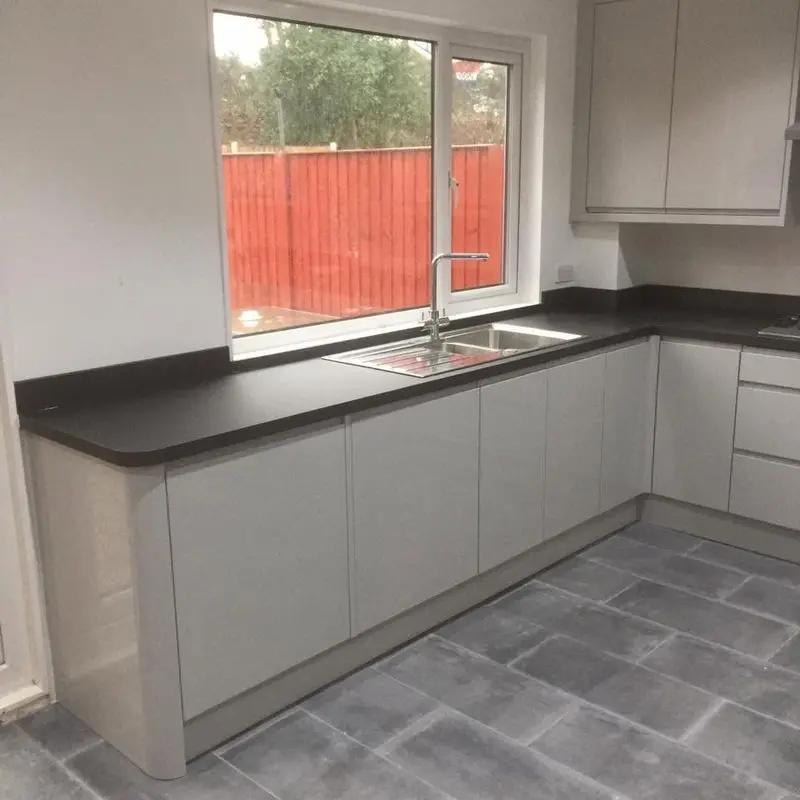 Light grey gloss handleless kitchen with dark worktops and a grey tiled floor