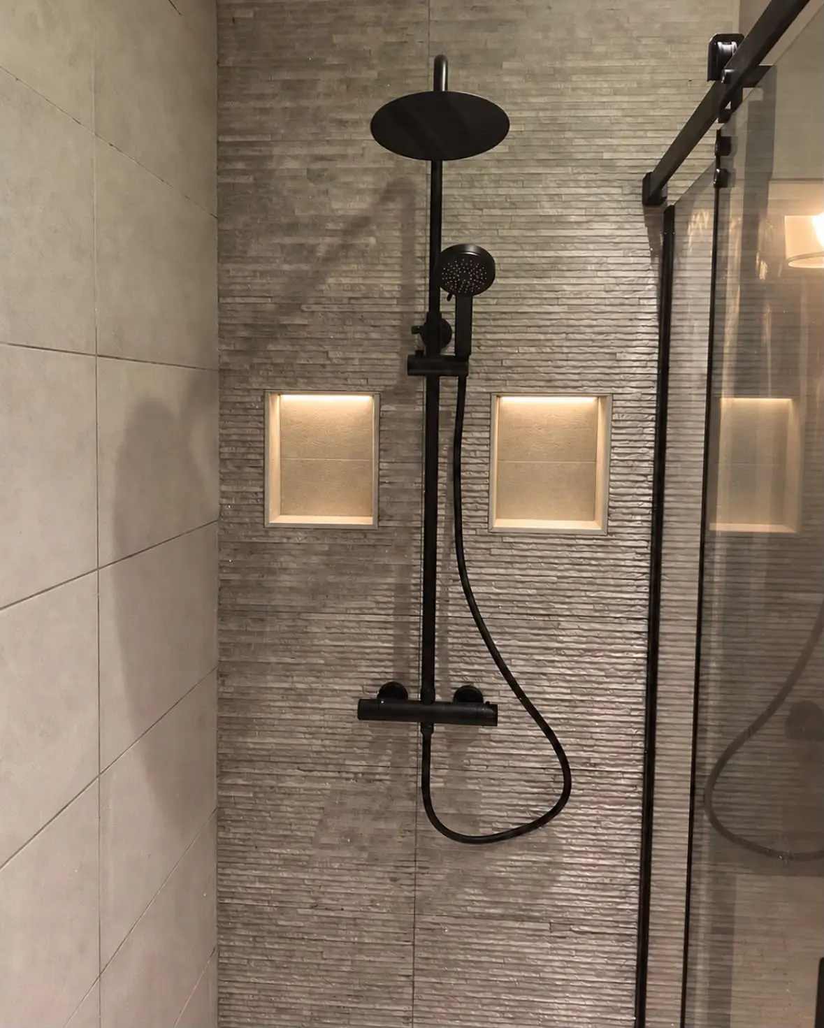 Walk-in shower with a black rain shower and two lit alcoves