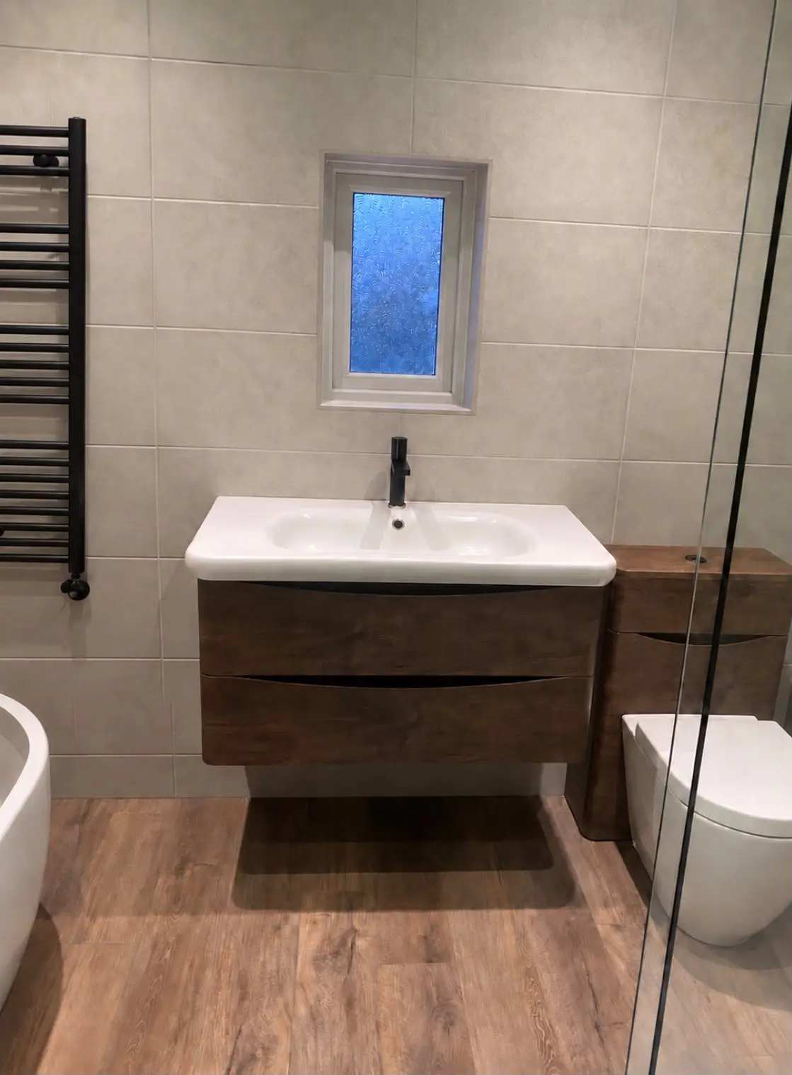 Wall-hung wood-effect vanity unit with a black tap, beneath the window