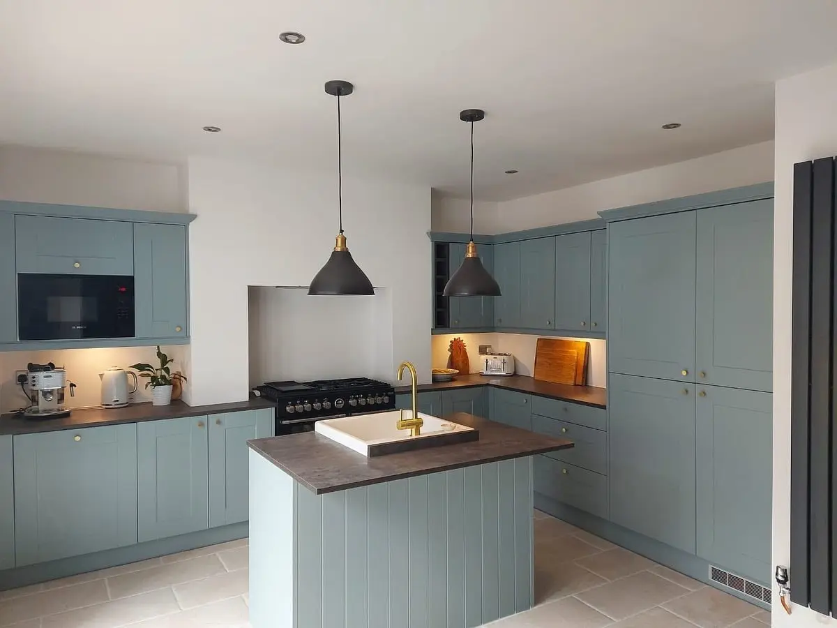 Blue-grey shaker kitchen with an island, brass tap, dark worktops and black pendant lights