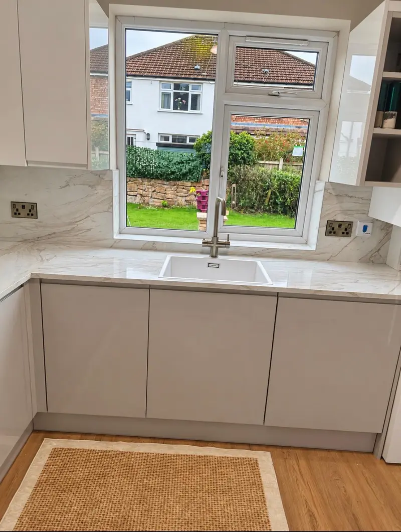 Grey gloss handleless sink run beneath the window, with a marble-effect worktop and splashback