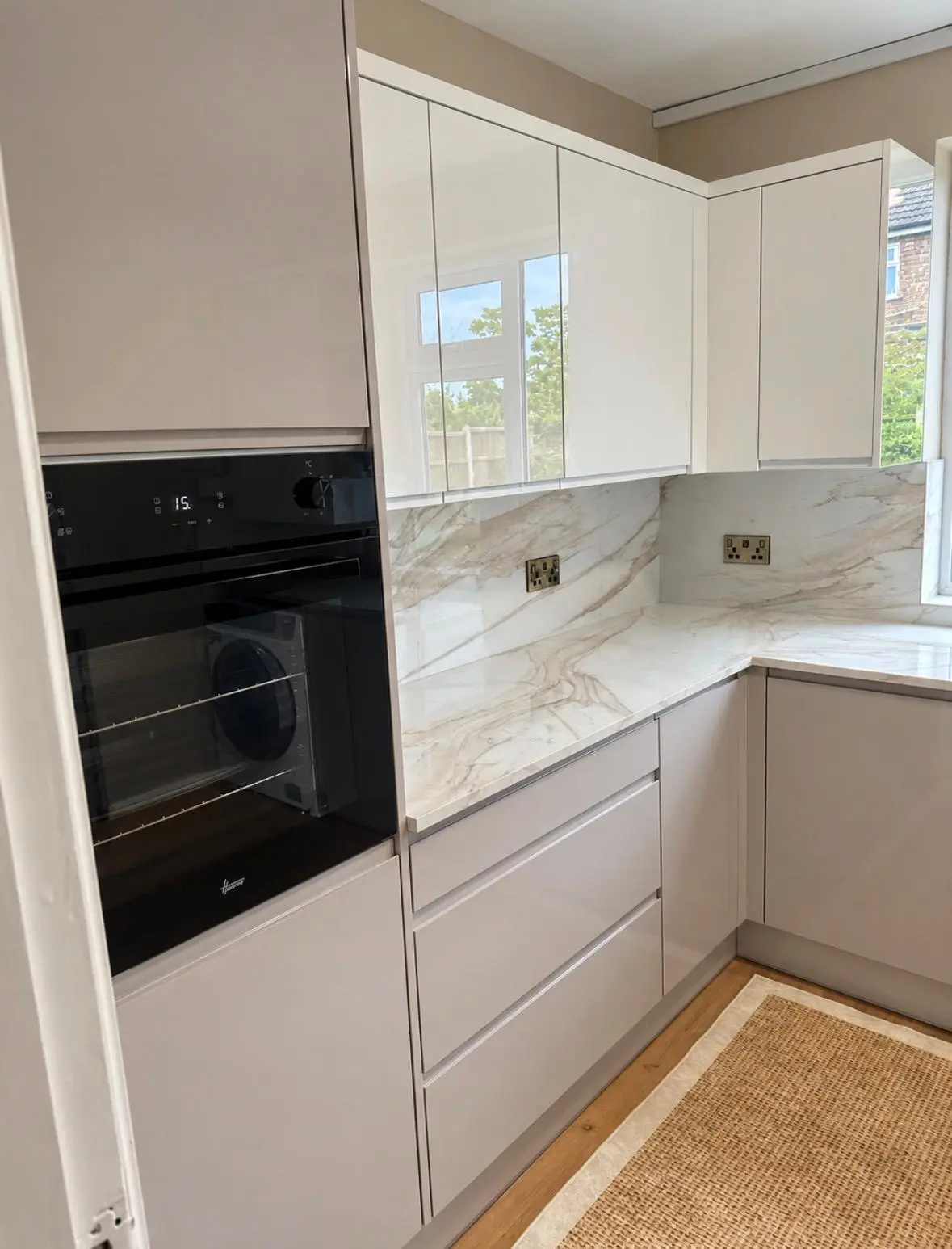 Built-in black oven in a tall housing beside grey handleless drawers and a marble-effect splashback