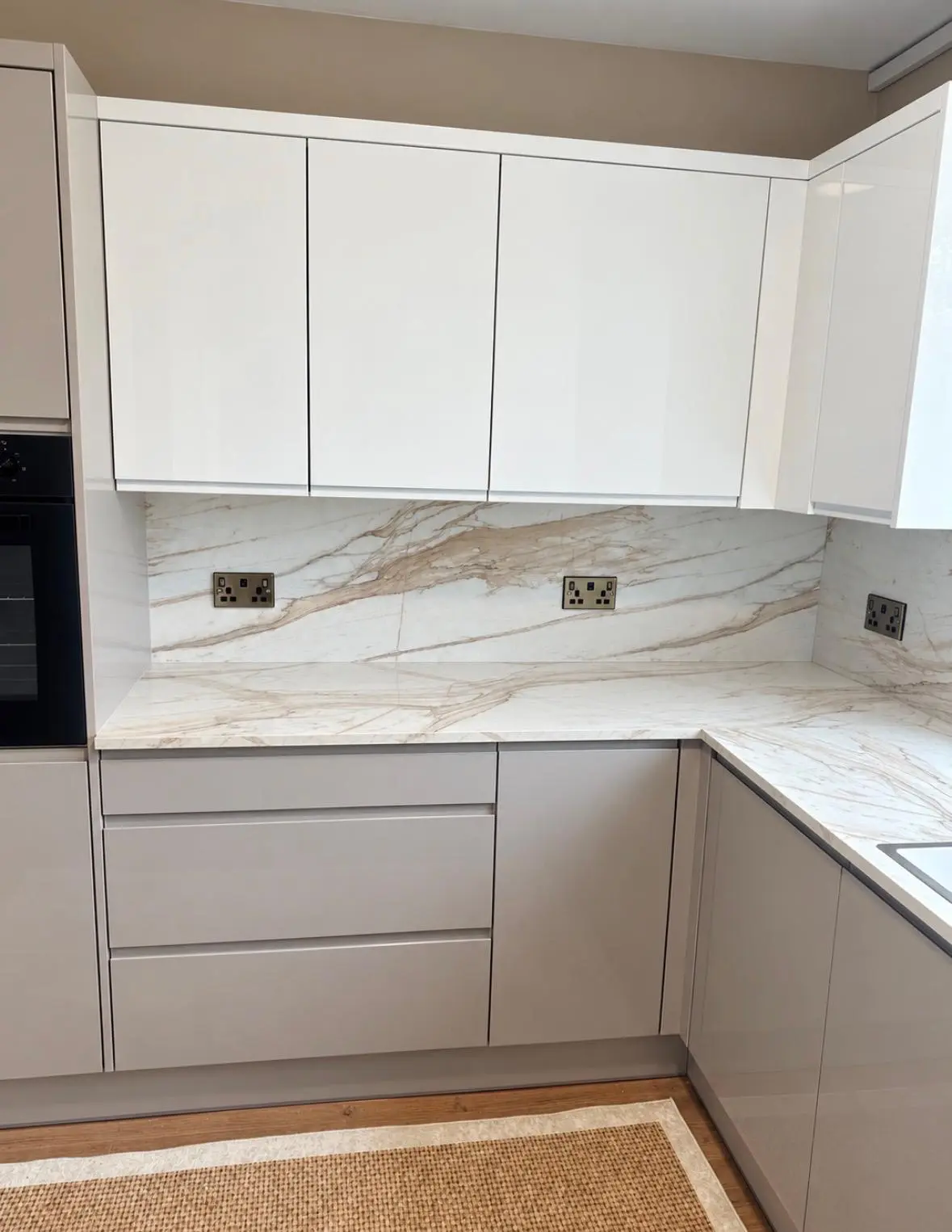 White gloss wall units over grey handleless base units with a marble-effect worktop and splashback