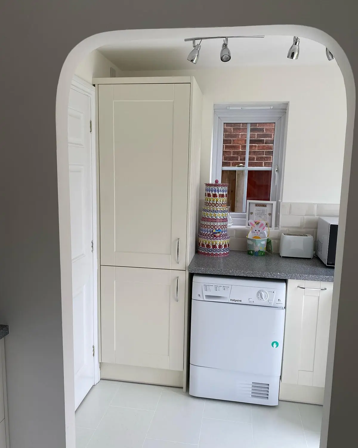 View through an arched doorway to cream shaker tall units and laundry appliances