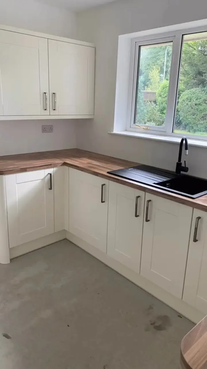 Cream shaker kitchen with oak-effect worktops, black handles and a black composite sink under the window
