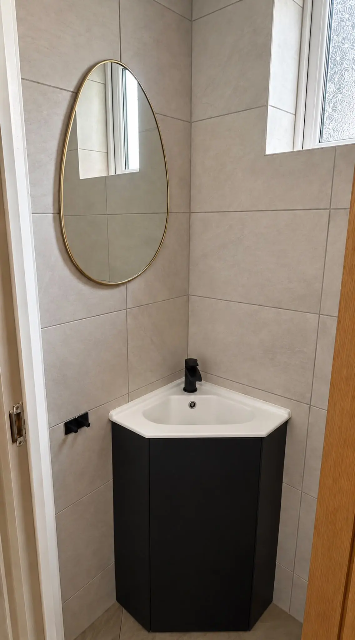Black corner vanity unit with a black tap beneath an oval mirror