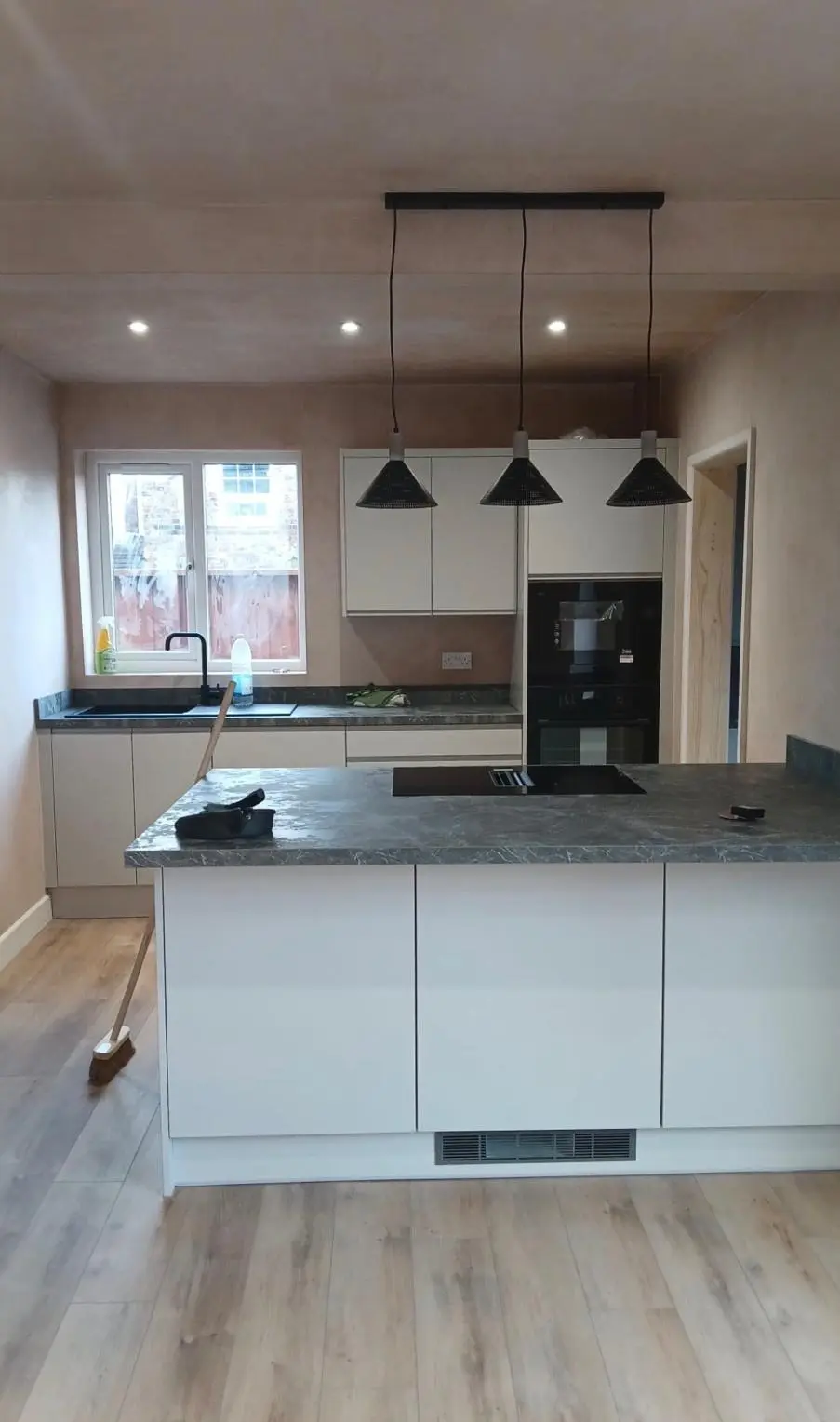 New kitchen fitted before decorating: island with downdraft hob, concrete-effect worktops and pendant lights