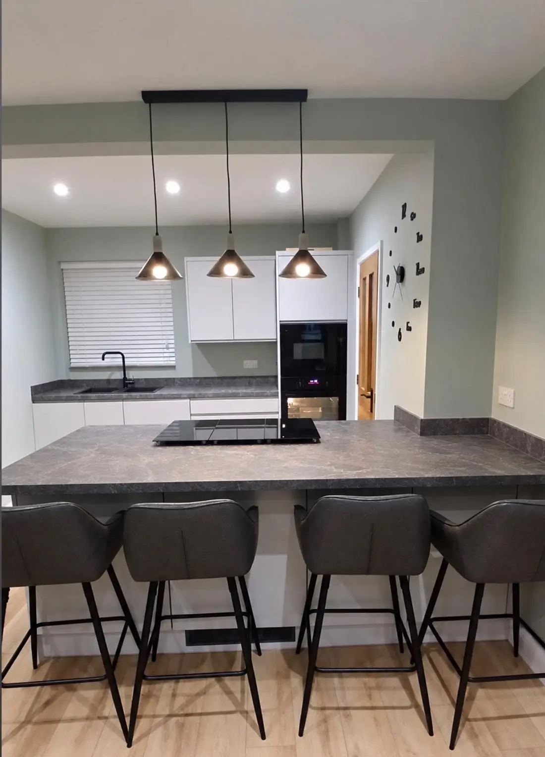 Island with breakfast-bar seating, a downdraft hob and three pendant lights in the open-plan kitchen