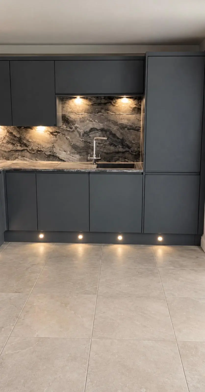 Lava grey kitchen seen across the tiled floor, with under-cabinet and plinth lighting