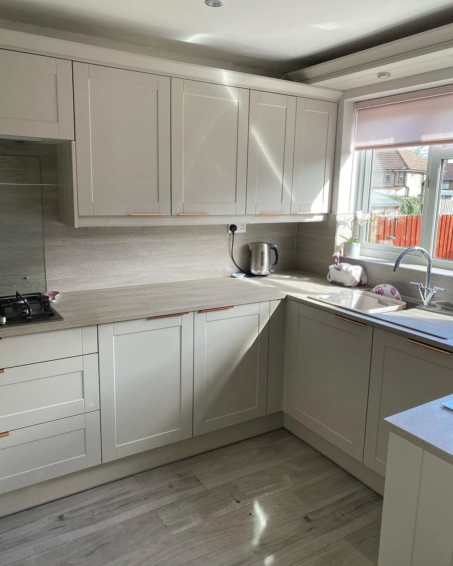 Light shaker kitchen with copper handles and grey wood-effect worktops, seen from the doorway