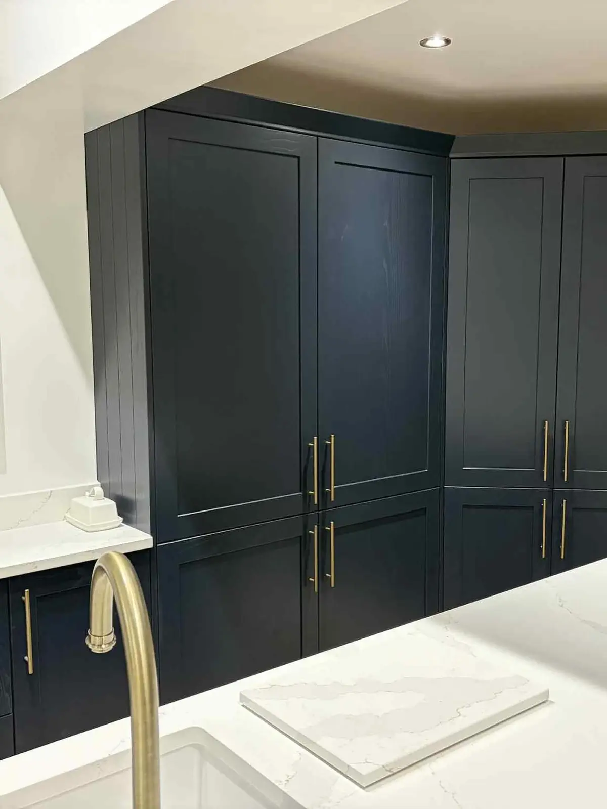 Close-up of navy shaker tall units with brass bar handles and a brass tap