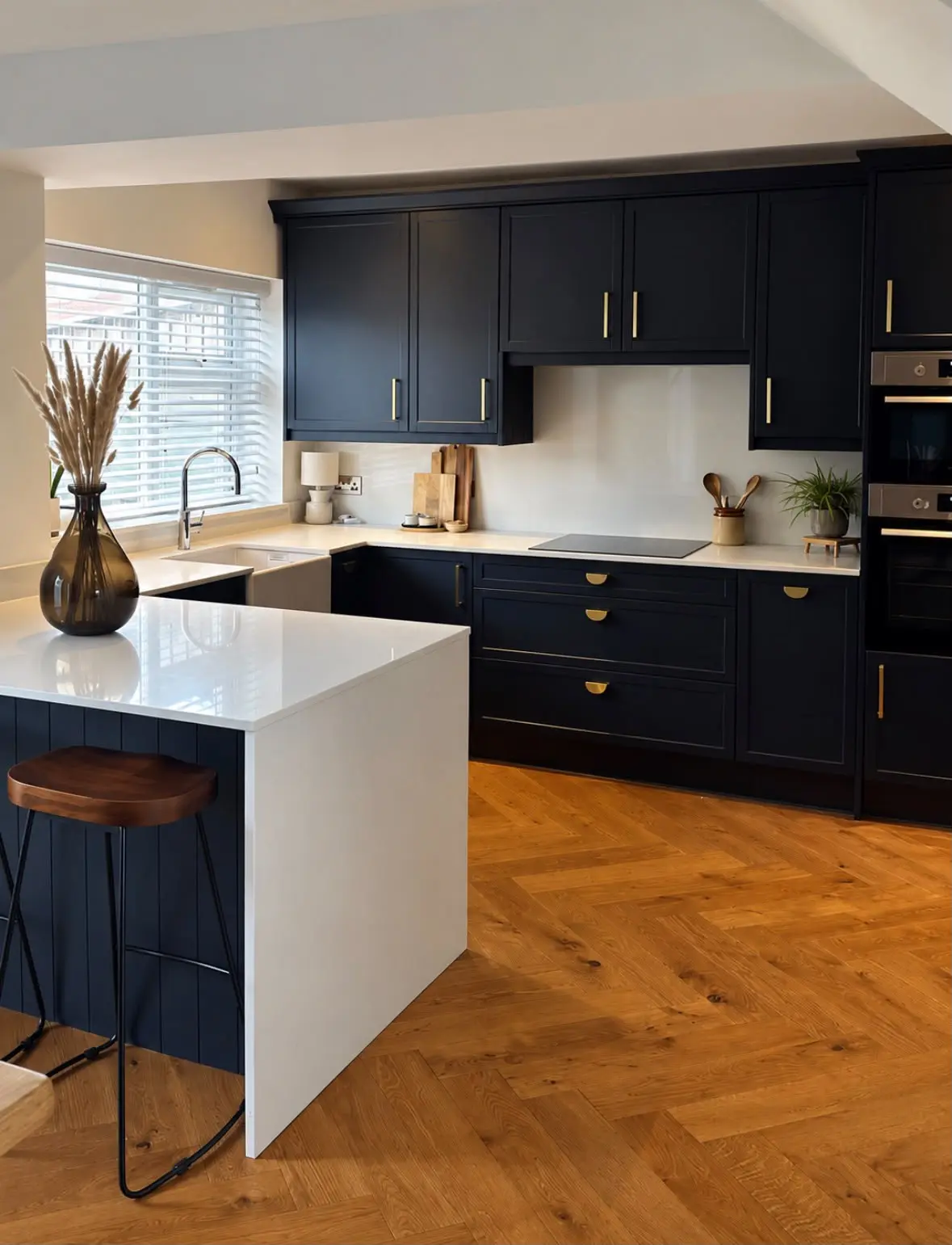 Navy shaker kitchen with a white quartz waterfall peninsula and bar stools on a herringbone wood floor