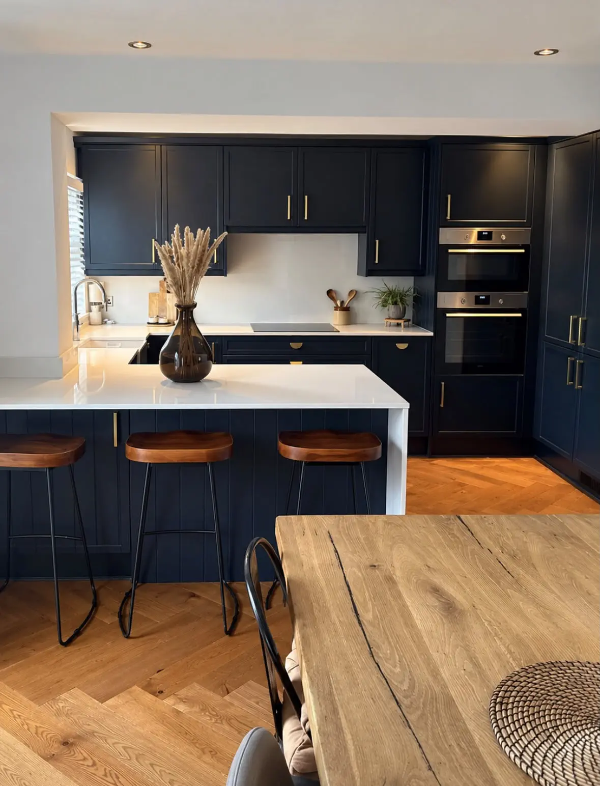 Navy shaker kitchen with a white quartz peninsula, bar stools and a solid oak dining table in the foreground