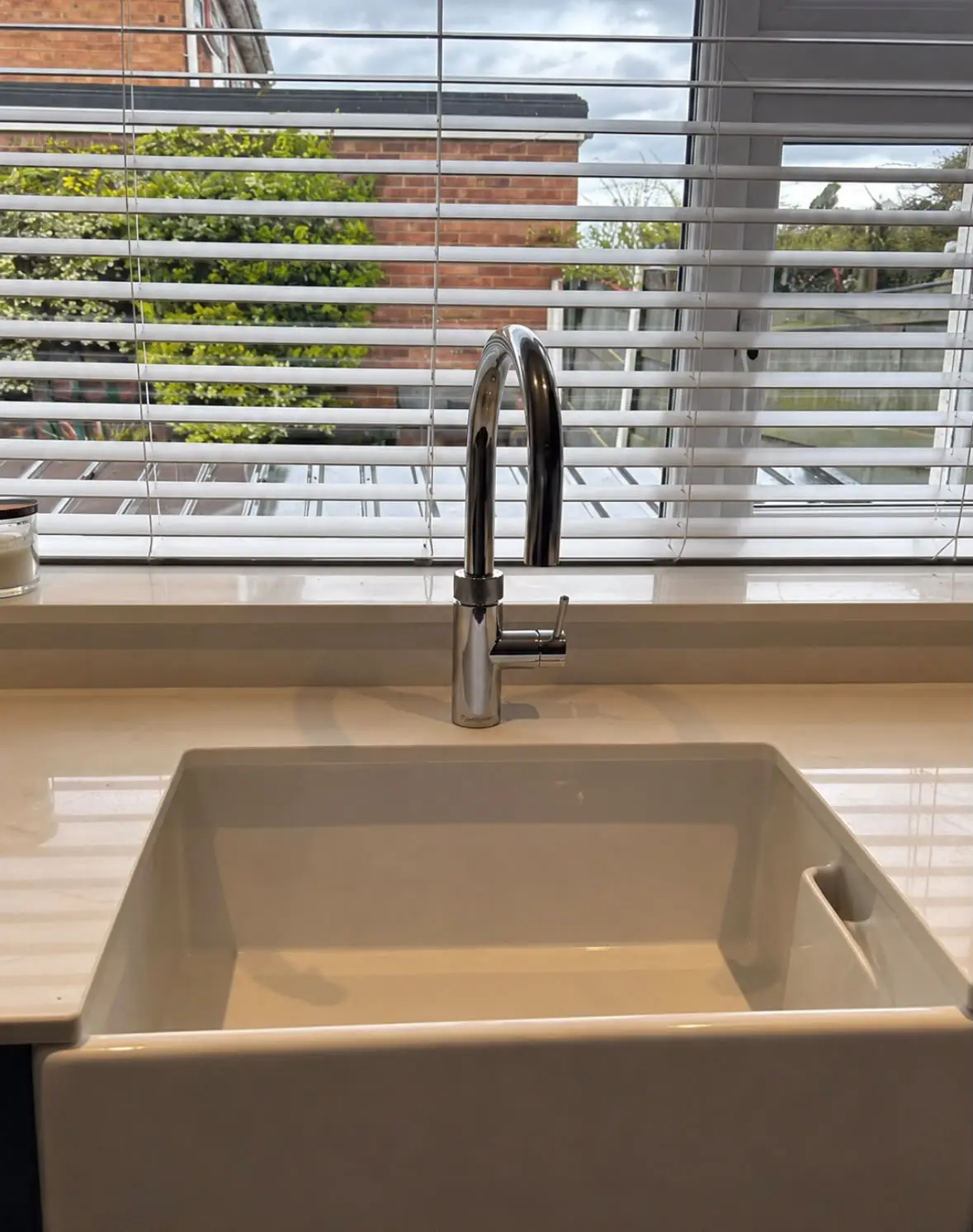 White ceramic sink with a swan-neck tap beneath the window