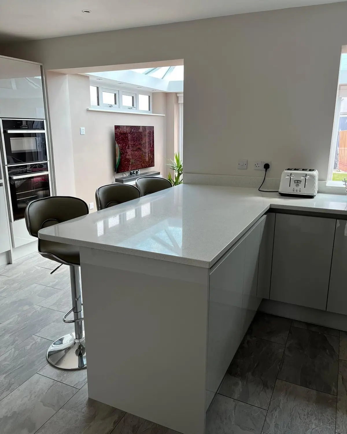 Handleless peninsula with white worktop leading into the living area