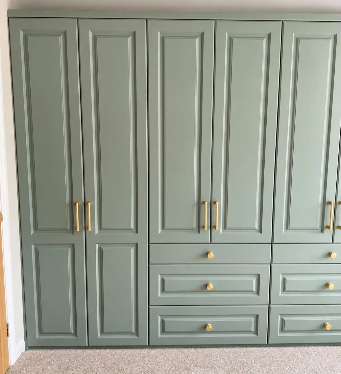 Run of sage green panelled fitted wardrobes with drawers and brass handles