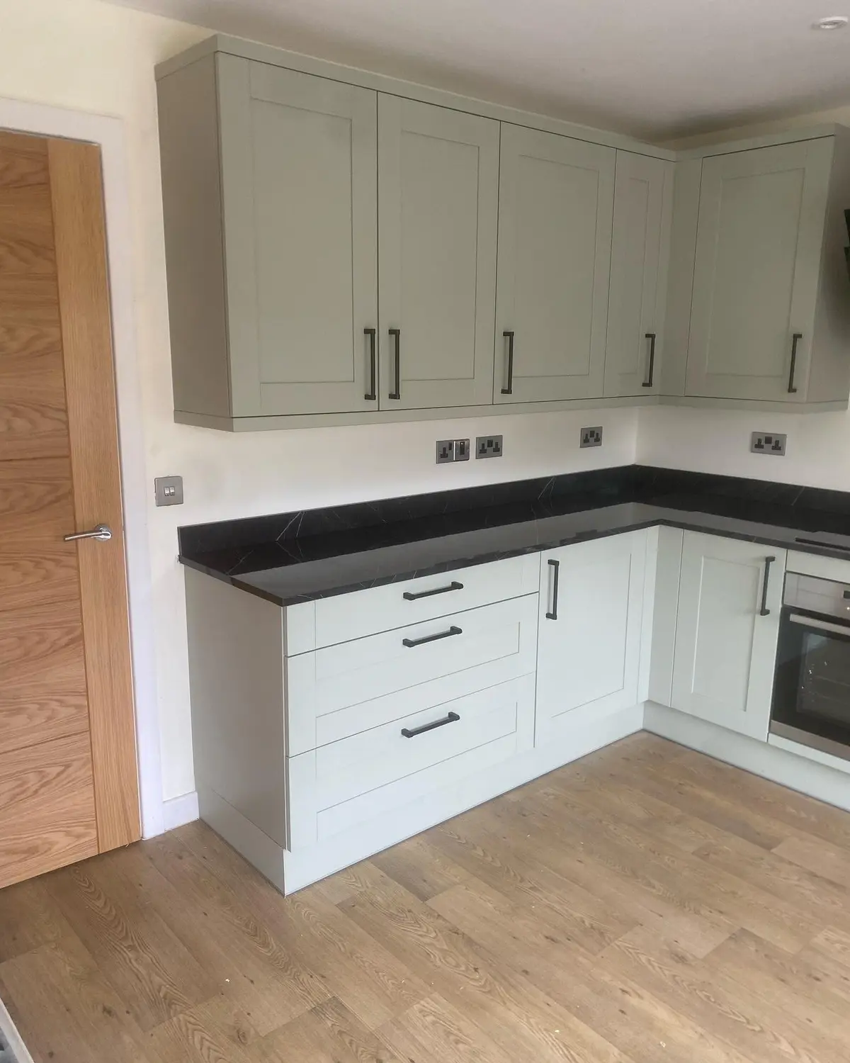 Sage green shaker kitchen with dark stone-effect worktops and a black angled extractor on a wood-effect floor