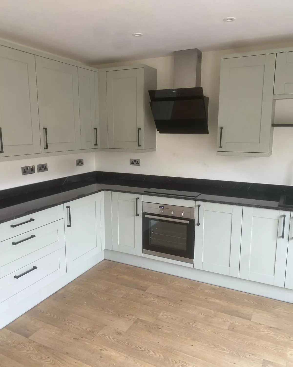 Sage shaker corner run with dark worktops beside an oak internal door
