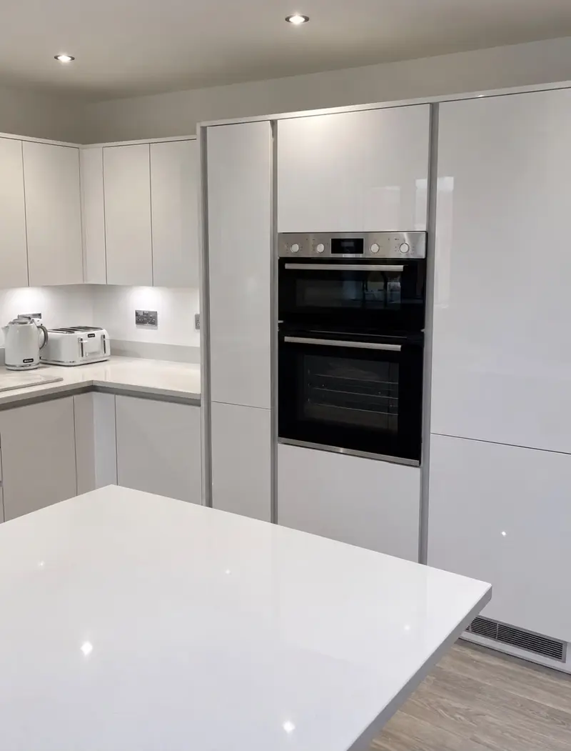White high-gloss handleless kitchen with stacked built-in ovens, an island and white worktops