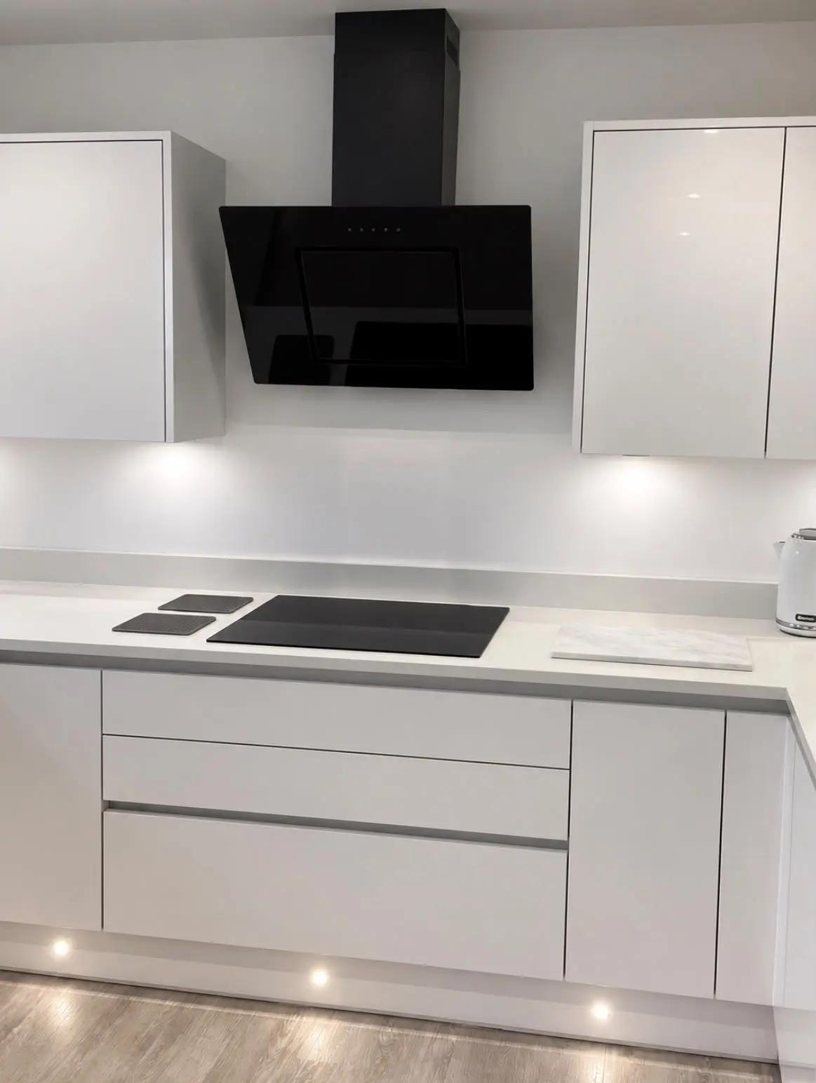 Hob beneath an angled black glass extractor, with pan drawers below
