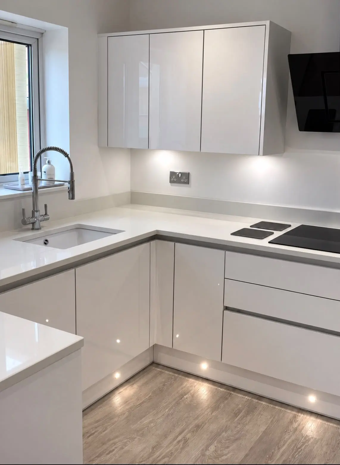 Sink run under the window with a spring tap, white worktops and plinth lights
