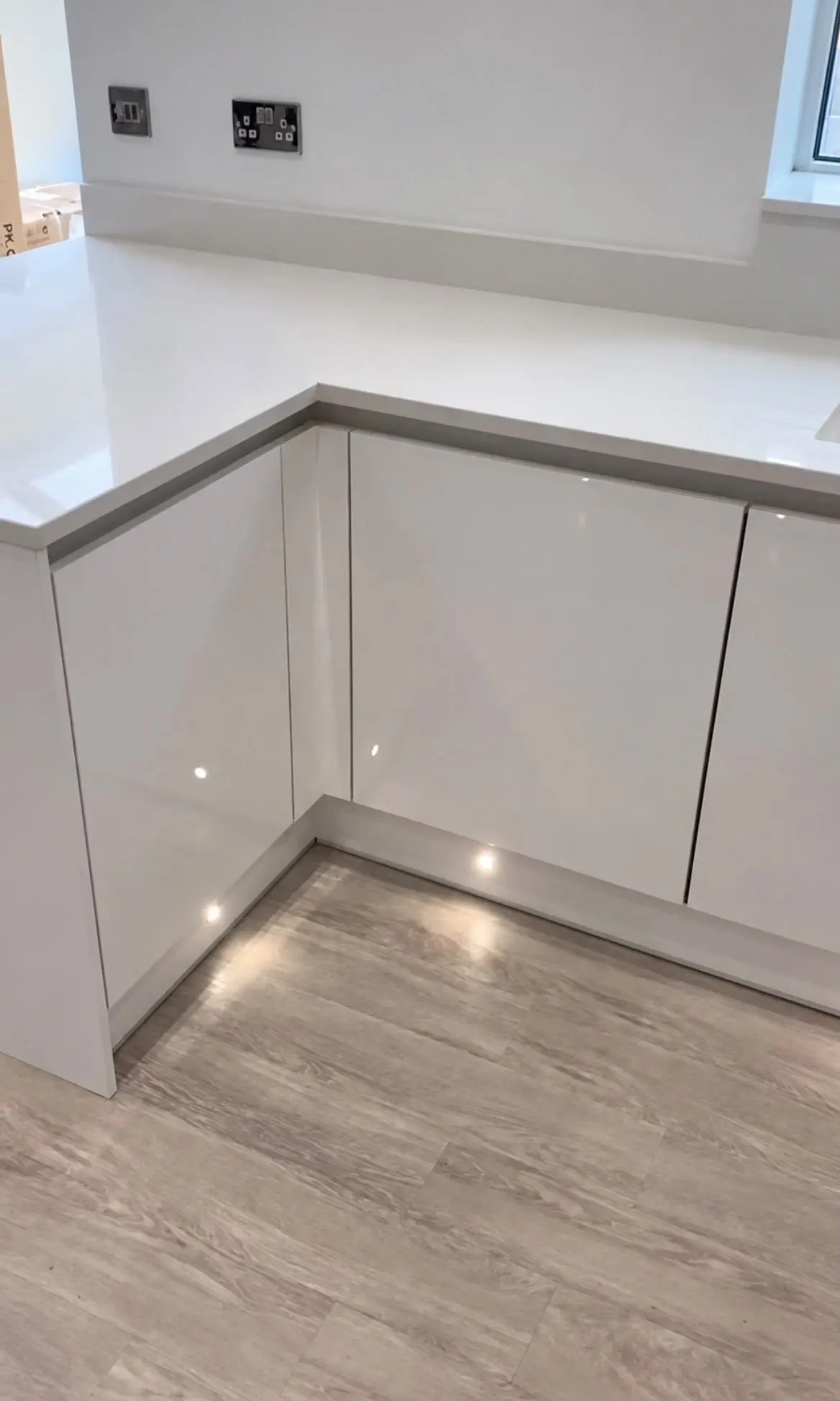 Corner of white gloss handleless base units with plinth lights on a wood-effect floor