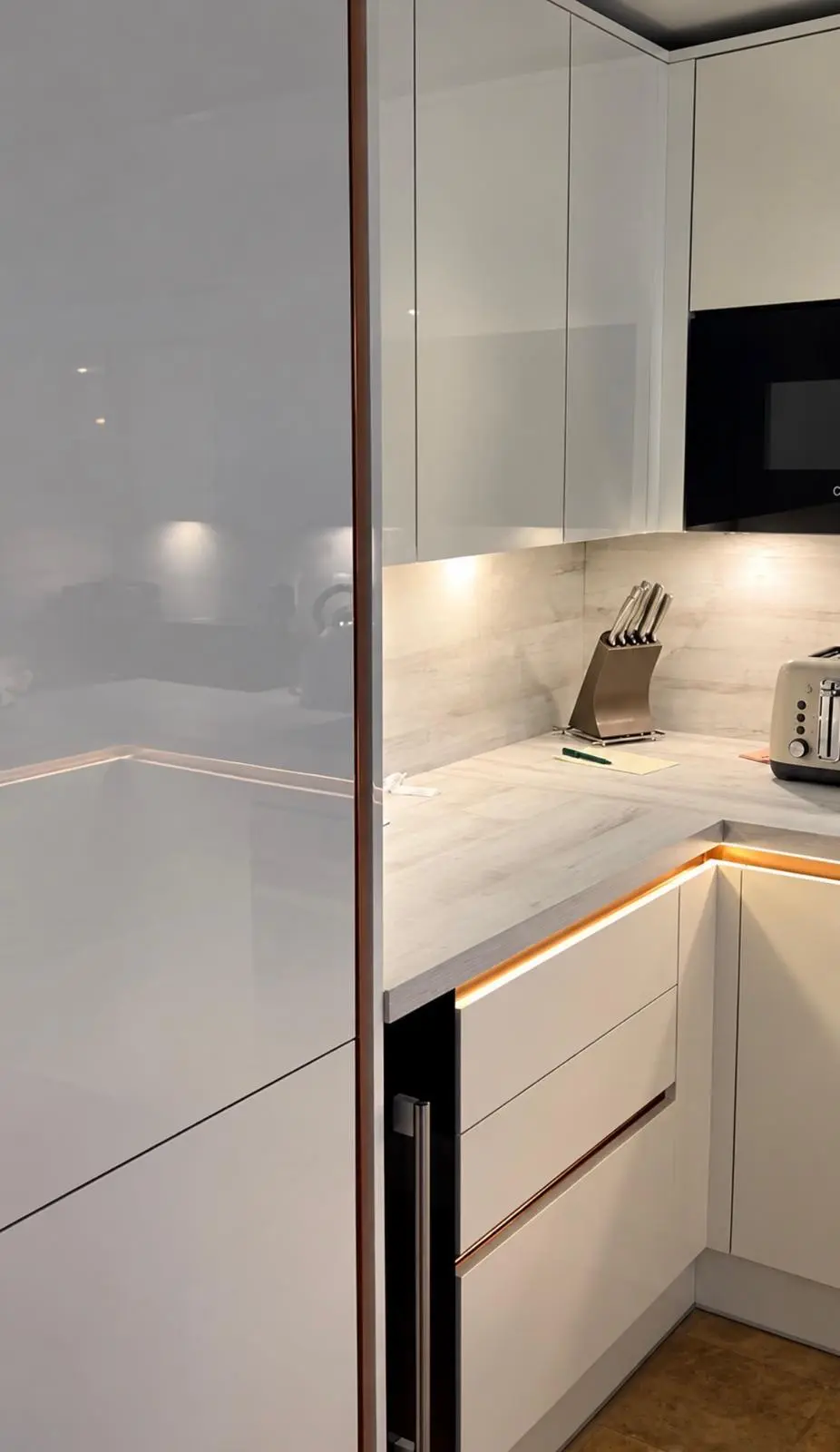 White gloss tall unit beside a corner run lit by warm white strip lights