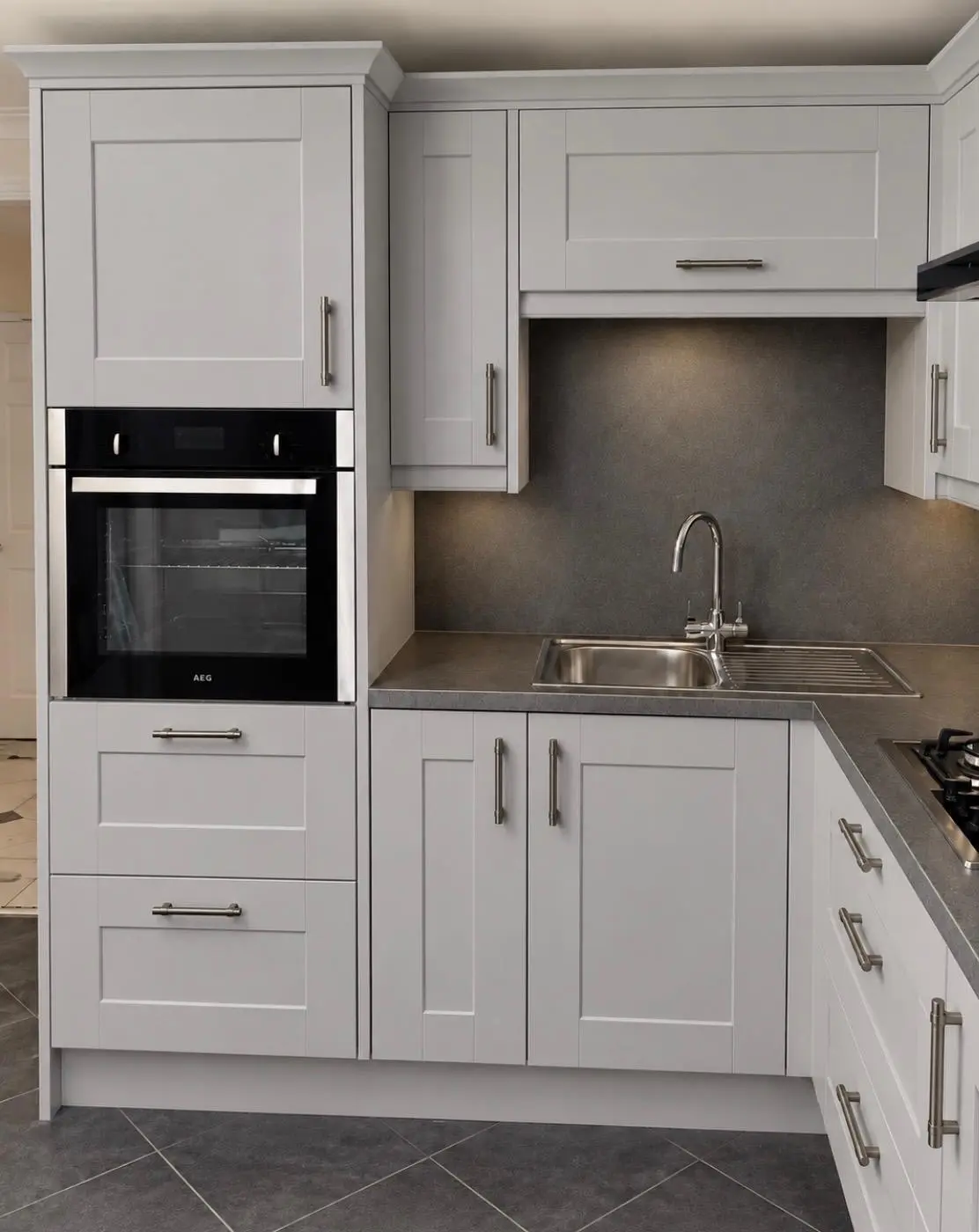 White shaker kitchen with built-in oven, sink and dark wall panels