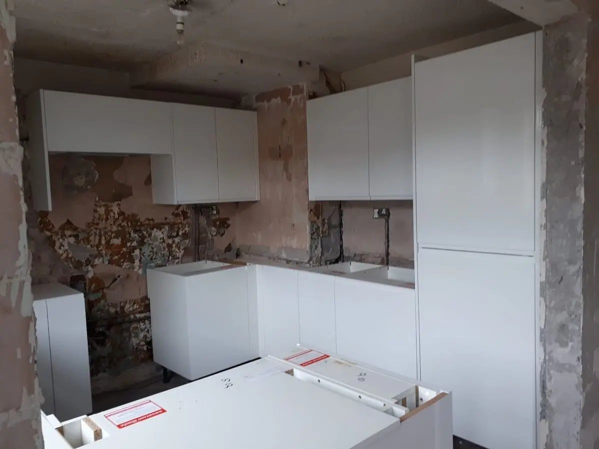 New white handleless units going in against the stripped walls, mid-installation