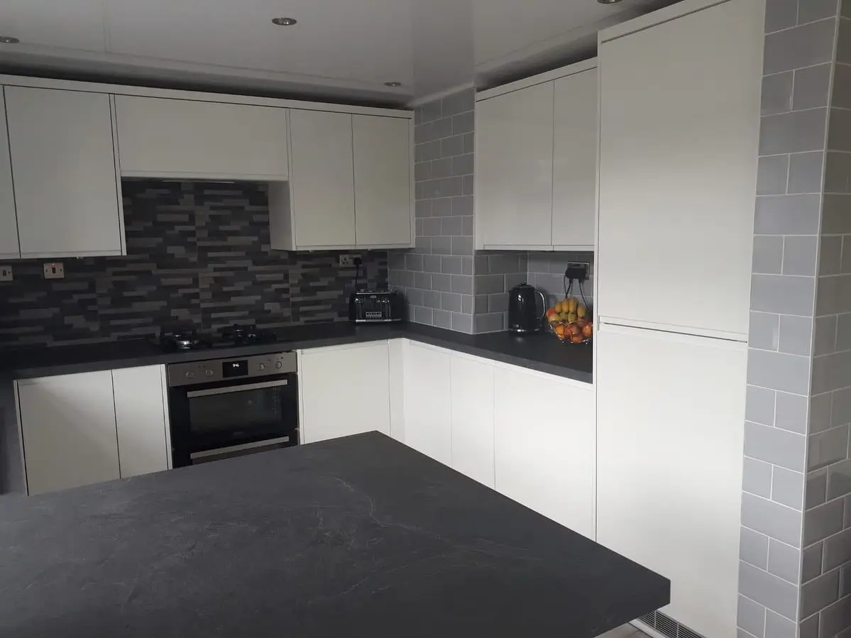 Finished white handleless kitchen with black laminate worktops and a grey and black mosaic splashback