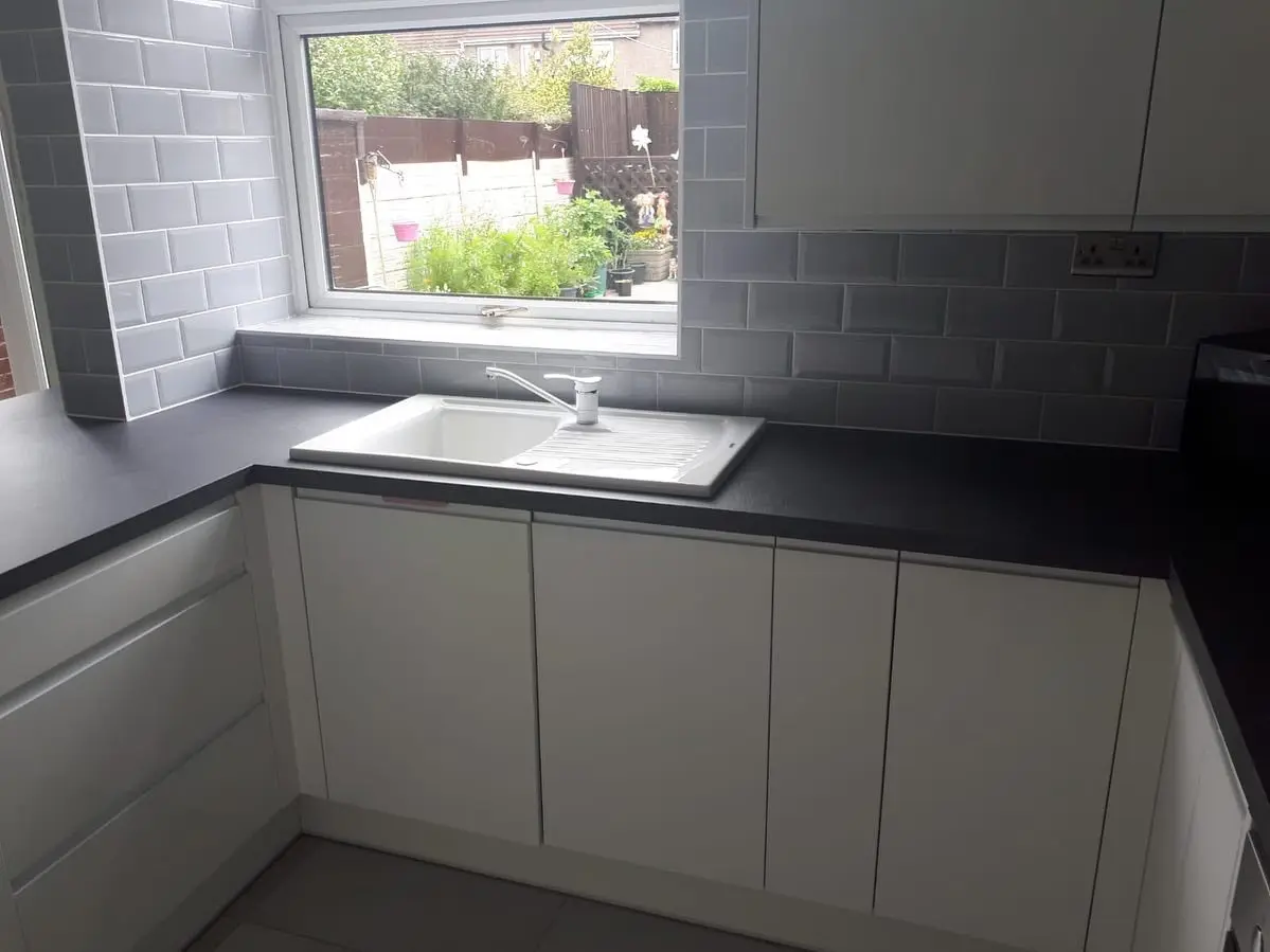 White handleless sink run under the window with black worktop and grey metro tiles