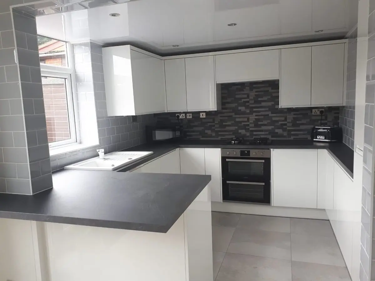 White handleless kitchen with black worktop peninsula, seen from the doorway