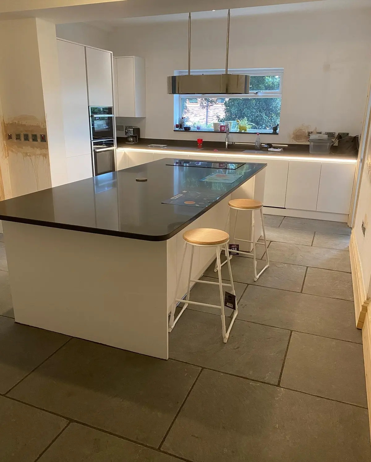 Large white handleless kitchen with a black quartz island, bar stools and pendant light over large-format floor tiles