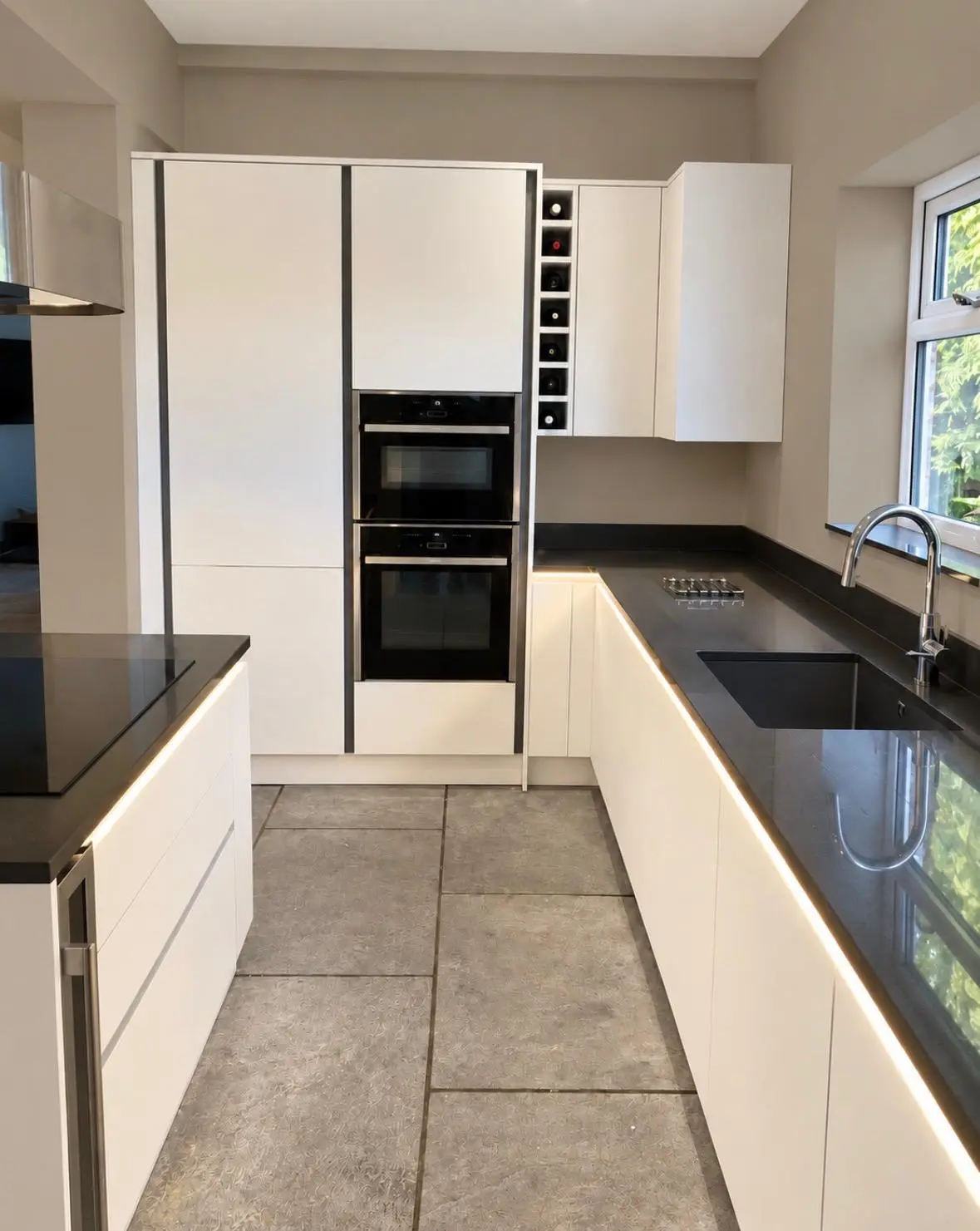 White handleless run with tall oven housing, black worktop and LED strip lighting along the base units