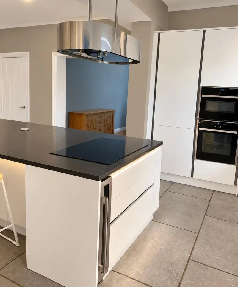 White handleless island with black quartz worktop, hob and strip lighting