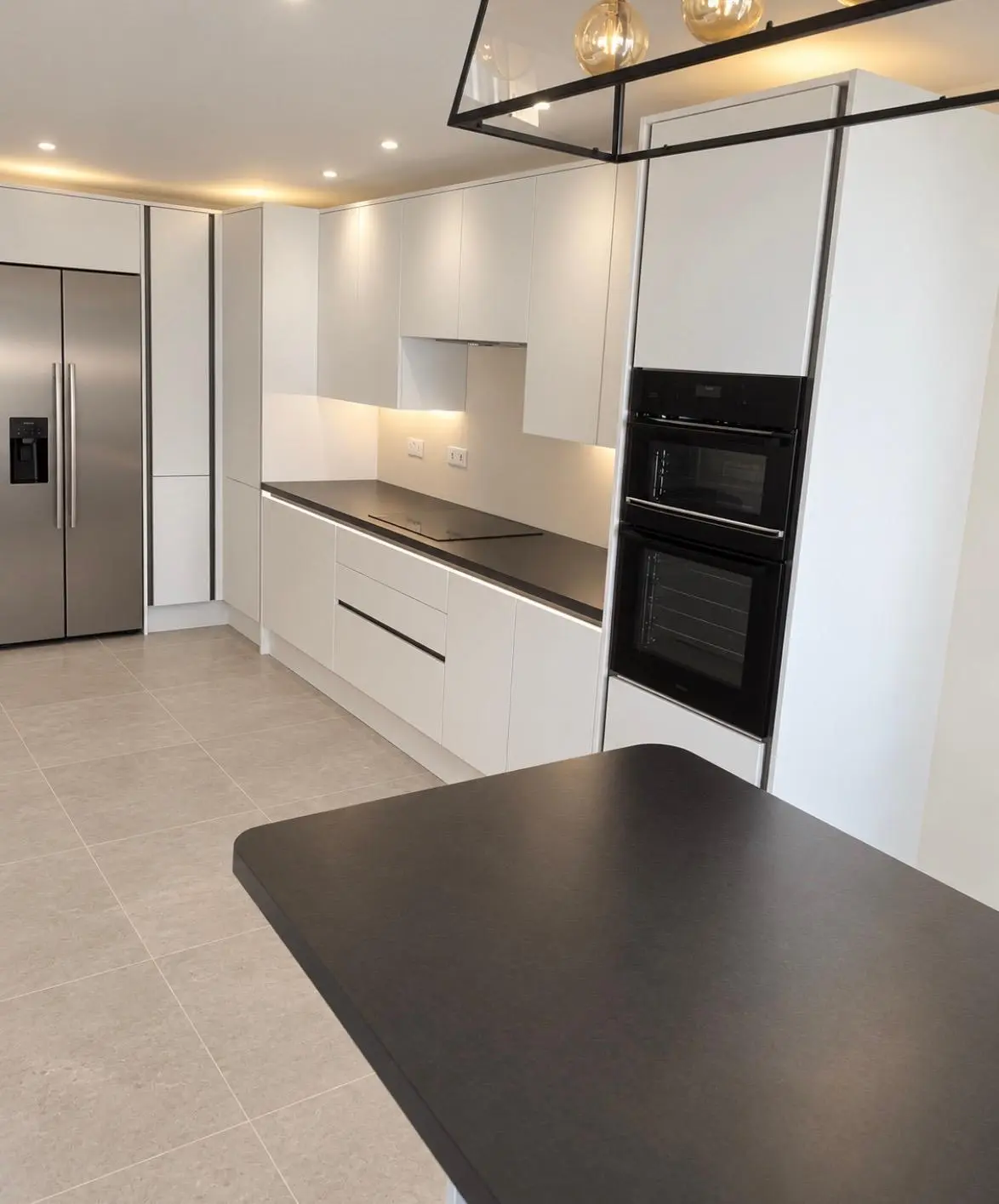 White handleless kitchen with a black-topped island, tall oven housing and American fridge freezer