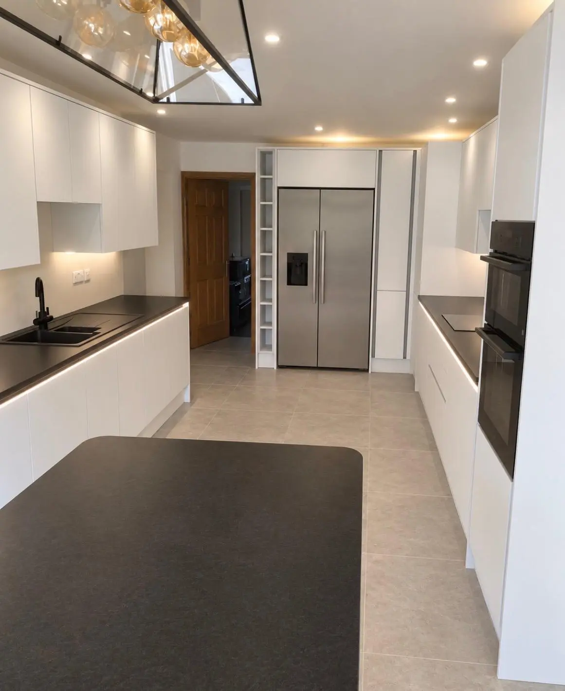 White handleless kitchen seen down the room toward the doorway, with the island in the foreground
