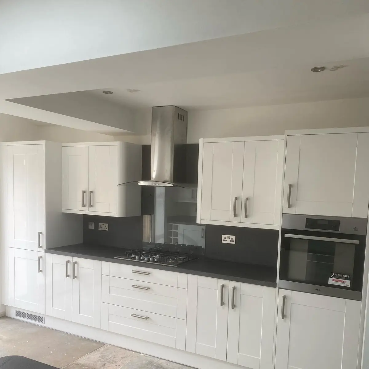 White shaker kitchen with grey worktop and stainless chimney extractor