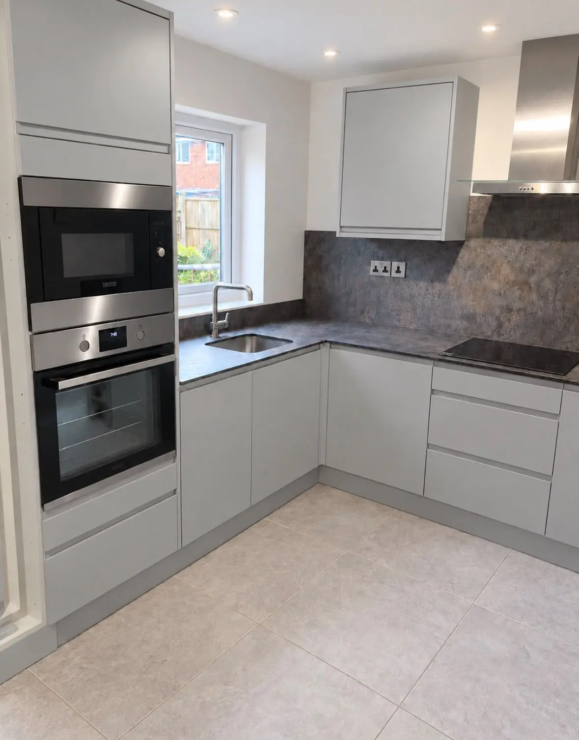 Grey J-pull handleless kitchen with a built-in oven and microwave and dark stone-effect worktops