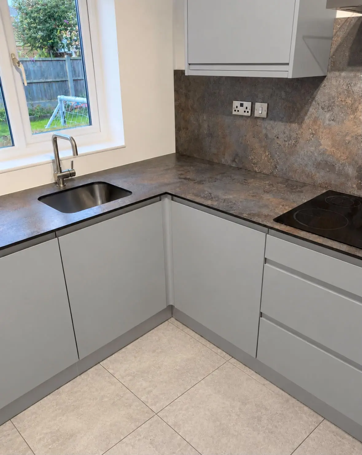 Undermount sink beneath the window, with grey J-pull drawers